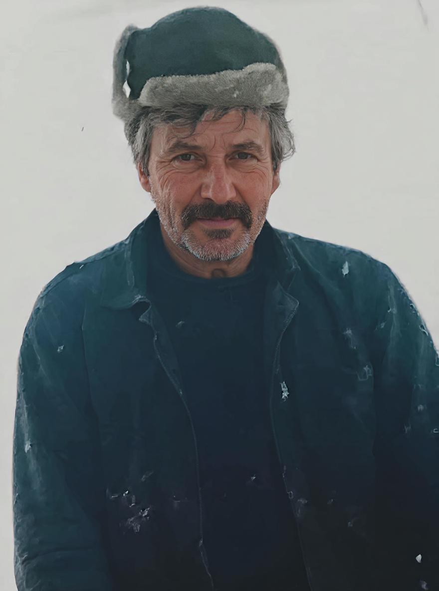 Focus solely on enhancing and restoring the man's body and clothing in this photograph. Do not change his face, expression, eyes, or hairstyle — preserve them exactly as they are. Sharpen and clarify the textures of his winter jacket (likely dark blue or green) and fur-lined hat, making the fabric and stitching look crisp and realistic. Enhance the folds, shadows, and natural wear of the clothing to give it depth and a lifelike appearance, as if photographed with a high-end DSLR. Retain the snowy background and lighting as is. No AI beautification, stylization, morphing, or changes to the man's identity — just detailed, high-quality restoration of the clothing and body posture.