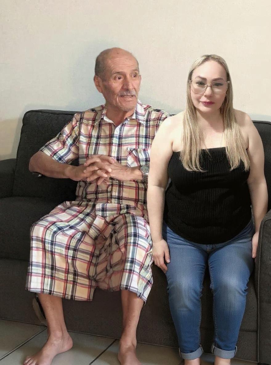 Pulir la imagen para que ambas personas sentadas en el sofá se vean completamente realistas, manteniendo exactamente sus rostros, parte superior del cuerpo y expresiones originales. Ajustar piernas y postura con proporciones correctas, agregar sombras naturales en el sofá y el piso, y suavizar la transición entre las partes originales y las generadas. Mantener la iluminación y el tono de color uniforme en toda la imagen."
