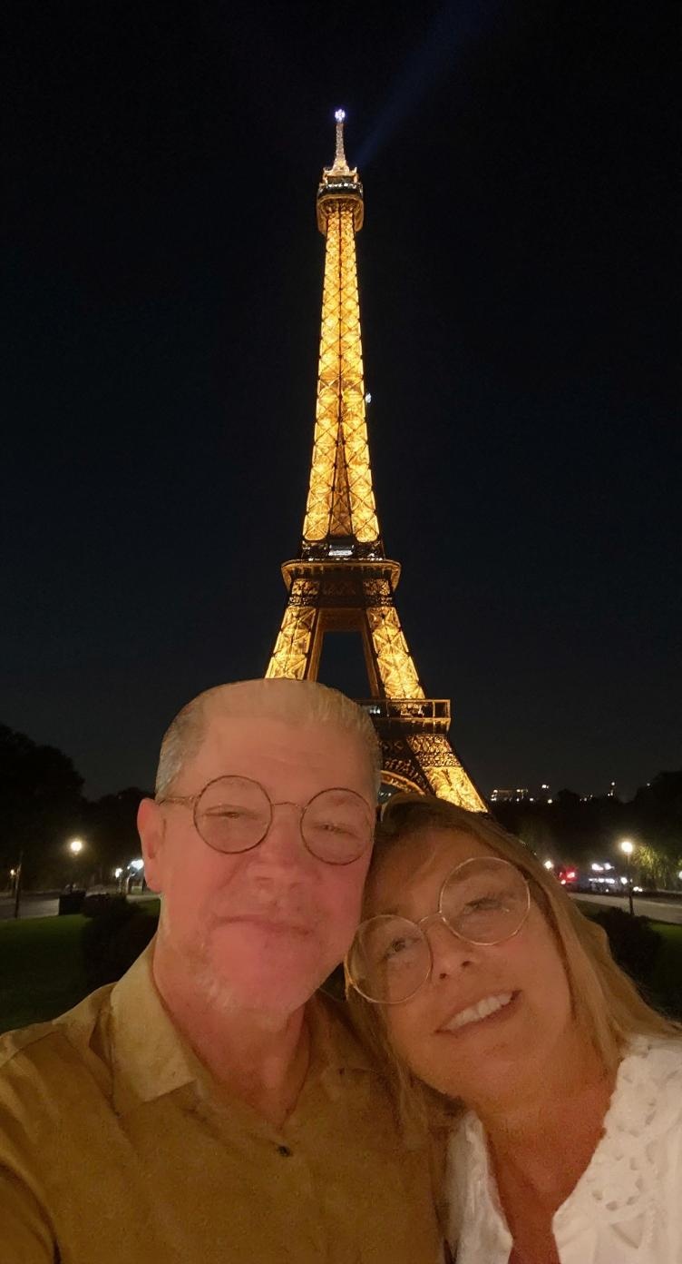 Gere uma imagem a partrir da imagem anexa  onde o casal está em frente a Torre Eiffel em uma viagem de verão a noite.
