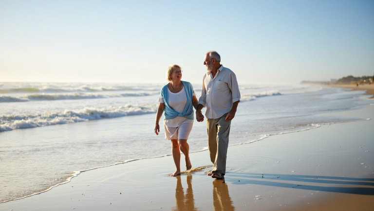 photograph of an elderly couple walking hand in hand on the beach